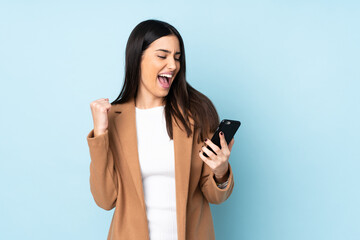 Young caucasian woman isolated on blue background with phone in victory position