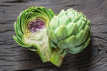 Green and purple artichoke flower edible buds on wooden background.