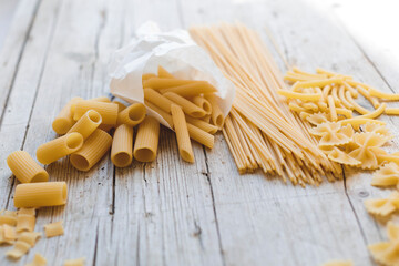 a lot of different kinds of egg noodles and yellow pasta on wooden background