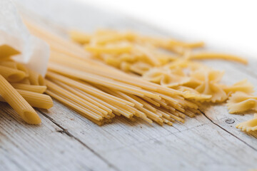 a lot of different kinds of egg noodles and yellow pasta on wooden background