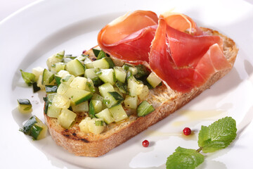 Sandwich with stewed zucchini and prosciutto meat on a white plate.