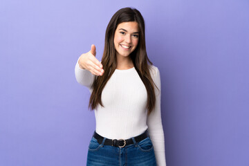 Fototapeta na wymiar Teenager Brazilian girl over isolated purple background shaking hands for closing a good deal