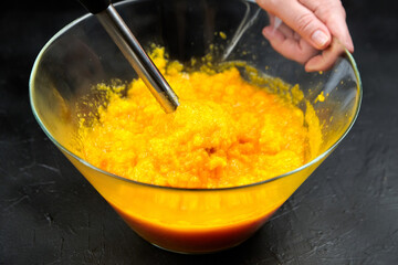 Woman cooking pumpkin puree with blender in glass bowl on black table. Mashed pumpkin. Healthy vegetable food