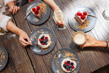 Bachelorette party, girls hands with drinks and sweet cakes with summer berries on a wooden table. Party, sweet table. Summer offer desserts in the restaurant.