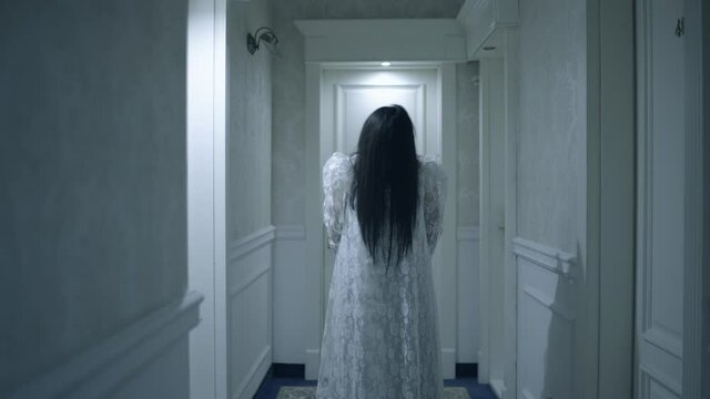 Witch in bride gown standing in dark hallway, face hidden in hair, black magic