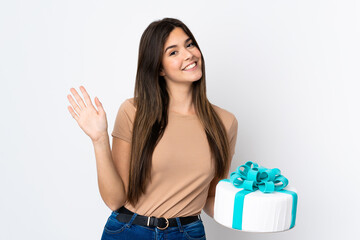 Teenager pastry chef holding a big cake over isolated white background saluting with hand with happy expression
