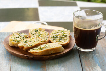 Garlic bread on the wooden plate with black coffee