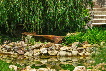 Wooden garden bench in the shape of half a circle by a rocky pond surrounded by greenery 