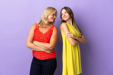 Mom and daughter isolated on purple background looking over the shoulder with a smile