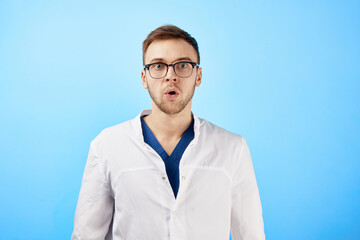 Shocked doctor in white coat opened his mouth in surprise isolated on blue background