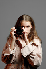 A girl photographer in a pink jacket holds a mirrorless camera in her hands.