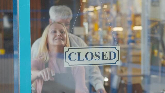 Two cheerful aged small business owners smiling while putting open sign at cafe entrance door