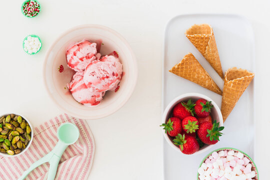 Dessert concept image with flat lay top view style against a white background with copy space.  Fresh fruit ice cream nuts and waffle cones included in food photo along side tableware and serving prop