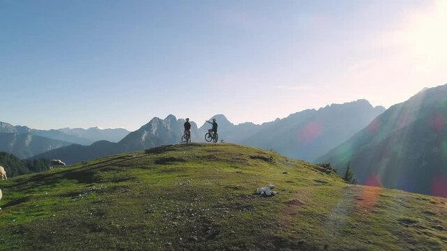 Aerial - Flying away from mountain bikers sitting on their bikes on top of beautiful Alpine mountain in spring