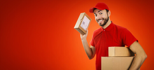funny delivery service man with box in hand on red background with copy space - obrazy, fototapety, plakaty