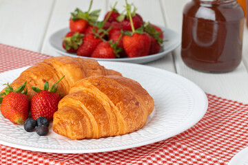 Fresh croissant decorated with berries on white wooden board