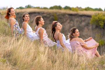 Naklejka premium A cheerful company of beautiful girls friends enjoy a picturesque panorama of the green hills at sunset