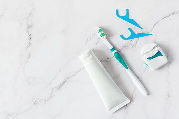 Toothbrush, toothpaste and dental floss top view on white marble background.