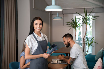Young waitress with payment terminal in restaurant