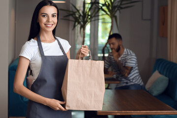 Young waitress with food for delivery in restaurant