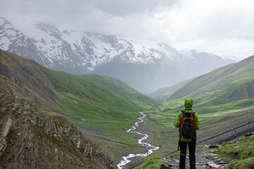 Trekking person in path with clouds, rain and bad weather covered in rain protective equipment in alpine mountain pass of the alps