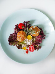 On a white plate cutlets with quail eggs decorated with herbs and tomatoes