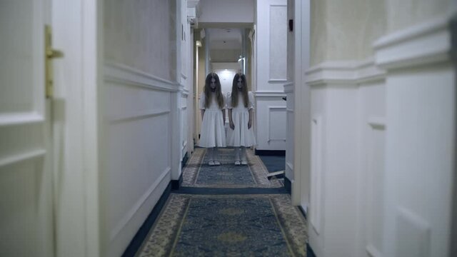 Spooky twin girls standing in empty hallway, strange atmosphere in haunted house