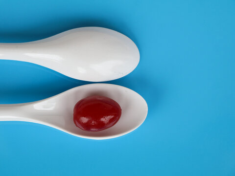 Red Color Cherry Fruits In A White Spoon Against Light Blue Background, With Copy Space, Caption