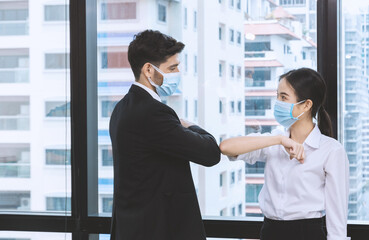 Office man and woman wearing face mask greeting by elbow bump.