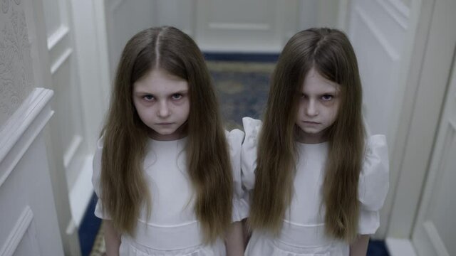 Strange pale twin girls seriously looking at cam, ghosts in haunted house