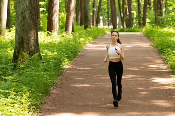 Jogging in nature. Girl in headphones runs in the park, smiling