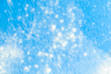 Snow spots are defocused on a heavenly background, scattered throughout the space unevenly, randomly. Winter background from white spots on a gently blue canvas.White-beige smeared lights on a azure
