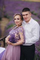 Young couple in love hugging in a lavender field on summer day. girl in a luxurious purple dress.