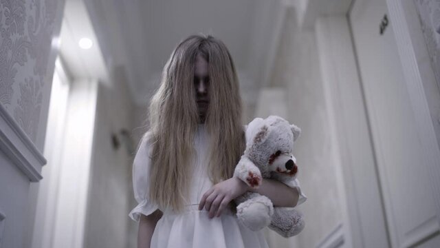 Possessed little girl holding bloody toy, standing alone in hallway, nightmare
