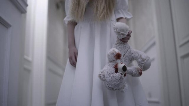 Possessed girl in white dress holding bloody toy, horrible sacrifice ritual