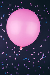 Pink balloon on a dark background with pink and blue round confetti. Festive background for your design. Flat lay, copy space, top view.