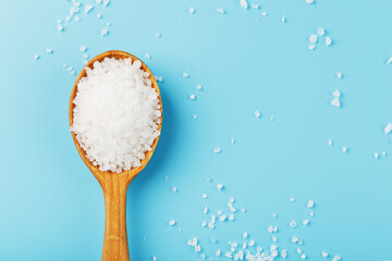 Sea salt in a wooden spoon on a blue background, with scattered salt.