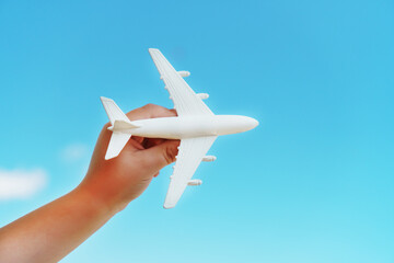 Naklejka na ściany i meble A white toy plane in a child's hand against a blue sky.