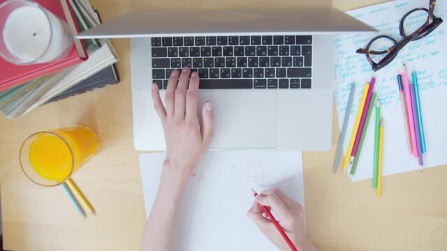 View from top women's hands typing on laptop keyboard on desk littered with papers and colored pencils the cat lies on table, office work home. Gesture hands Yes, winner
