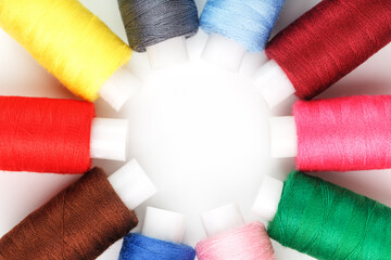 Sewing threads of different colors on reels on a white background in a circle.