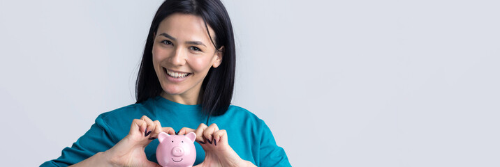 The girl holds a pink piggy bank and a coin in her hands. The concept of wealth and accumulation.