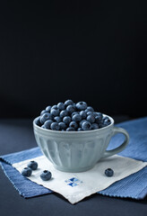 A cup o fresh tasty blueberries on a napkin and black background.