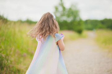 A little girl in a rainbow dress dress with a bouquet of wild flowers in her hands runs on the road in a field in summer. A girl enjoys a walk in the Park.