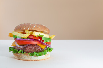 Fresh juicy beef hamburger with french fries placed on beige and brown creative trendy background