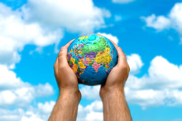 Human hands holds world globe planet earth on blurred blue sky and clouds background wallpaper.