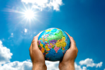 Human hands holds world globe planet earth on blurred blue sky sun and clouds background wallpaper.