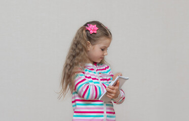 A portrait of a fair-haired schoolgirl stands with a notebook in her hands and writes in it. Light grey Studio background. Education. copy place