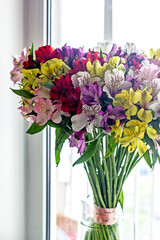 Alstroemeria bouquet of flowers in a vase by the window. Beautiful bouquet of colorful flowers in the apartment by the window.