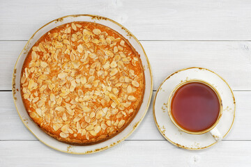 Homemade gooseberry pie garnished with almond petals and cup of tea on white wooden table. Top view.