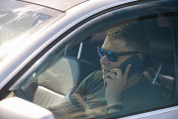 Driver is talking on mobile phone by a steering wheel of car.